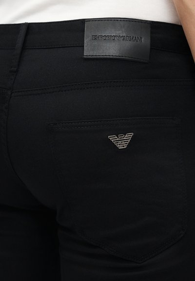 Μαύρα τζιν Emporio Armani με δερμάτινη ετικέτα της μάρκας στη μέση και μεταλλικό λογότυπο αετού στην πίσω τσέπη.