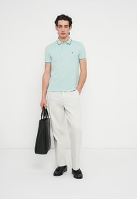 Ανοιχτό μπλε πόλο μπλουζάκι με αντίθετο γιακά και φάσα, σε συνδυασμό με λευκό παντελόνι και μαύρα παπούτσια, κρατώντας μαύρη τσάντα tote.