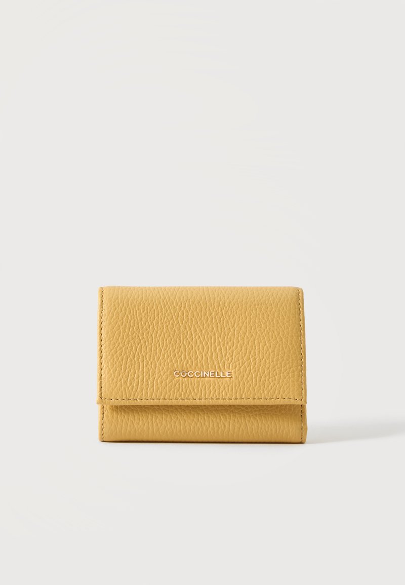 Petit portefeuille en cuir jaune texturé avec rabat avant et nom de marque métallique « Coccinelle » sur fond blanc uni.
