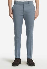 Ljusblå byxor i en mjuk textur, raka ben och sidofickor, i kombination med mörkbruna mockaskor.