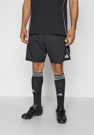 Shorts de sport noirs avec des accents roses, associés à des chaussettes noires montantes avec des rayures blanches et un logo, et des chaussures de foot noires.