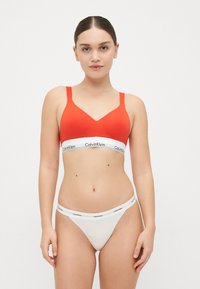 Červený bavlněný bralet s širokým bílým pásem Calvin Klein. Bílé tanga se shodným pasem. Hladká textura, jednoduchý design a přiléhavý střih.