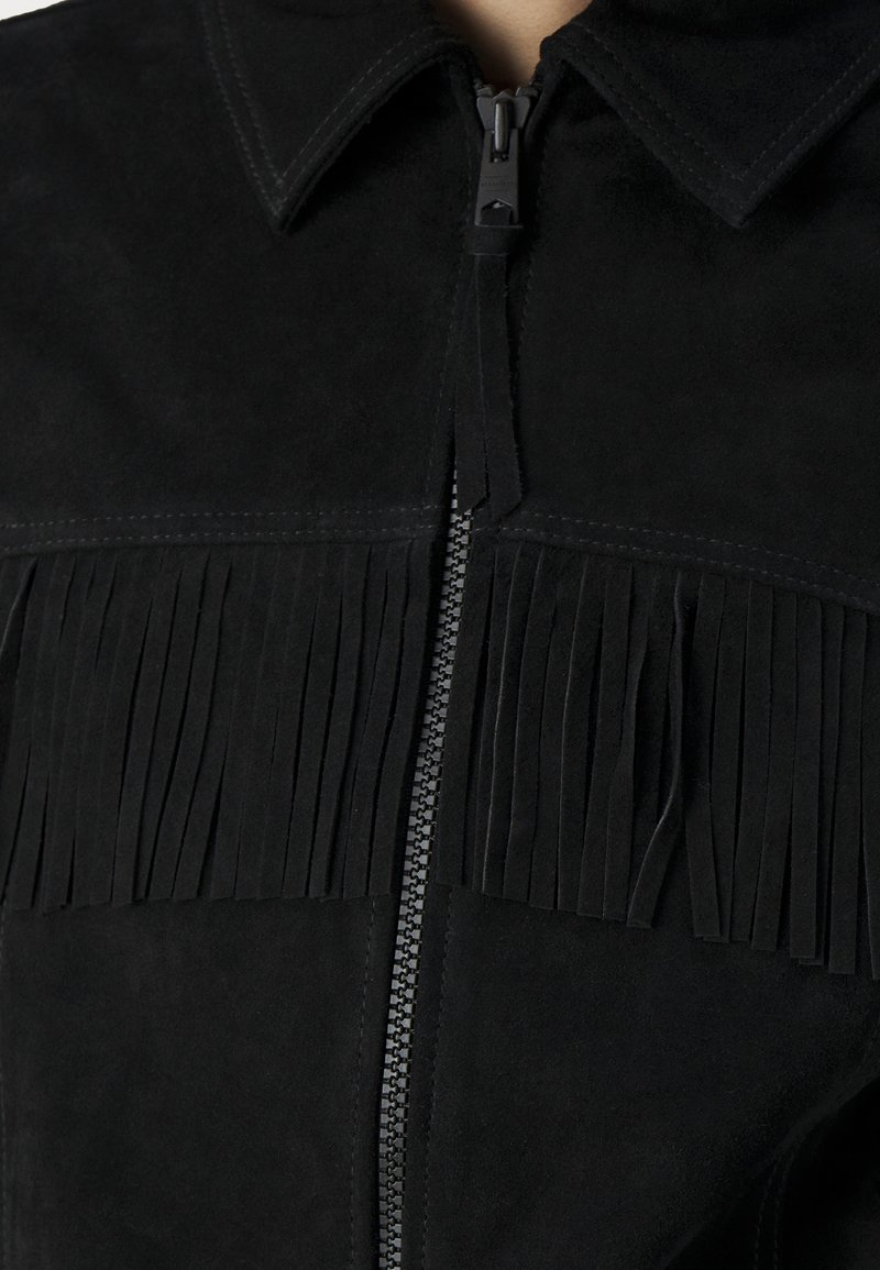 Veste en daim noir avec fermeture éclair, col pointu et franges verticales sur le panneau avant. Texture douce avec un fini mat.