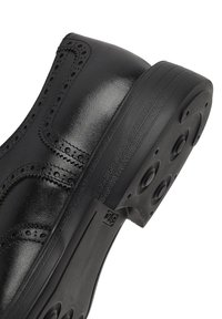 Zwarte leren schoen met brogue-details, ronde neus en een gestructureerde rubberen zool met ronde accenten. Gladde afwerking op de bovenkant.
