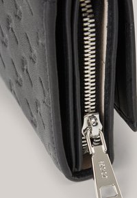 Schwarze, strukturierte Geldbörse mit einem Reißverschluss und silberfarbener Hardware, die ein schlankes Design und eine glatte Oberfläche präsentiert.