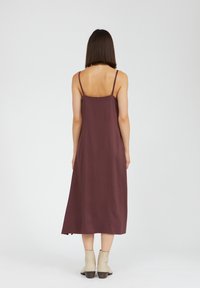 Burgundin midi mekko ohuilla olkaimilla, suoralinjaisella siluetilla ja sileällä pinnalla. Yhdistetty beigeihin nilkkureihin, vaaleaa taustaa vasten.