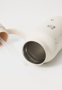 Gobelet en acier inoxydable avec un extérieur crème, un motif floral et une poignée rose clair. Comprend une paille en plastique transparent et un revêtement intérieur en métal.