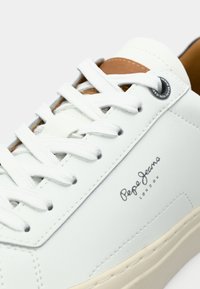 Close-up of white Pepe Jeans London sneaker with white laces, brown tongue, and beige sole.