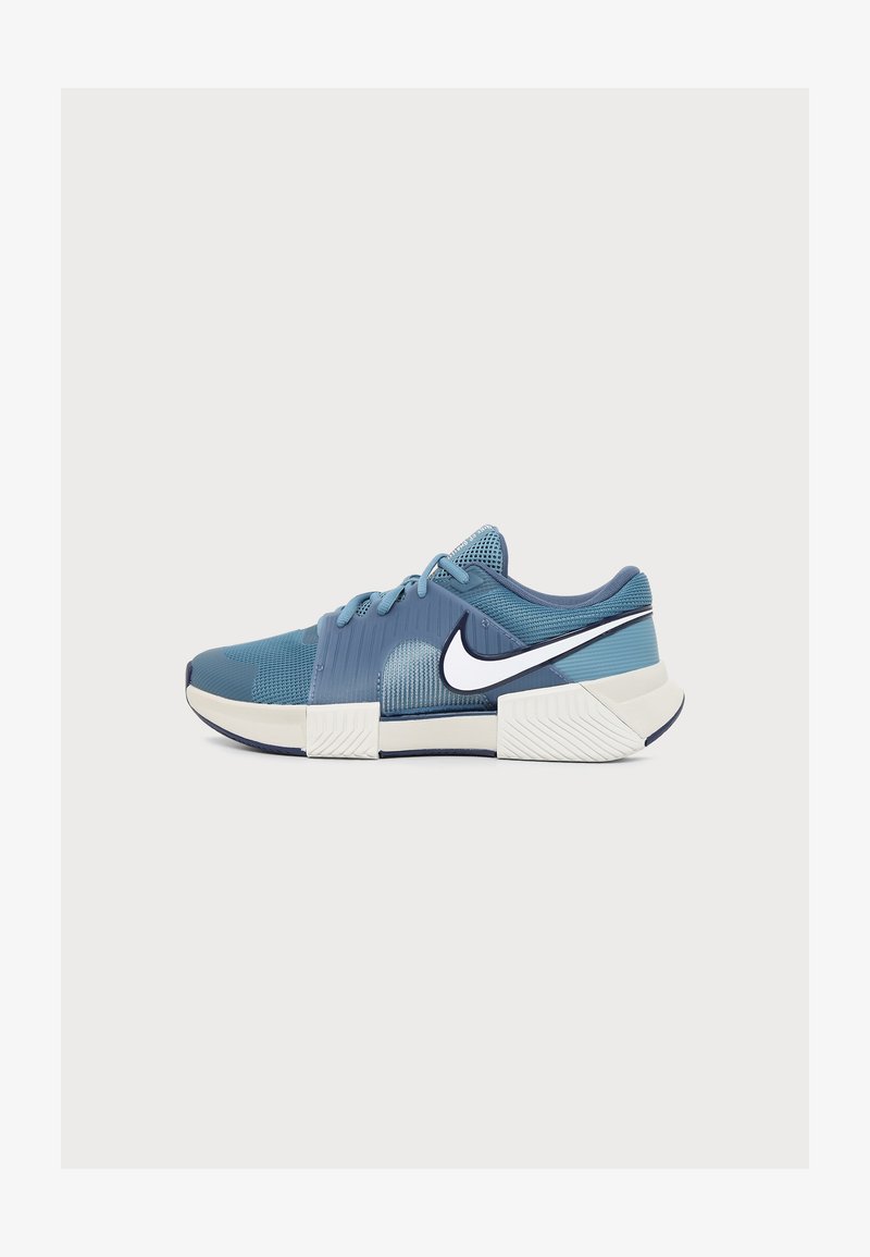 Μπλε και άσπρο αθλητικό παπούτσι Nike με επάνω μέρος από δίχτυ, κορδόνια, παχιά τμηματική σόλα και λευκό λογότυπο Swoosh με μαύρο περίγραμμα στο πλάι.