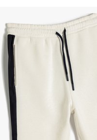 Cremefarvede joggers med sorte sidelstænger. Har en elastisk talje, justerbare snøringer og sidelommer. Blød tekstur.
