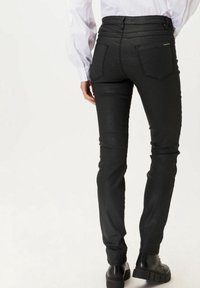 Pantalones vaqueros skinny negros de denim con una textura suave, cintura de altura media y dos bolsillos traseros. Terminados con detalles sutiles de la marca.