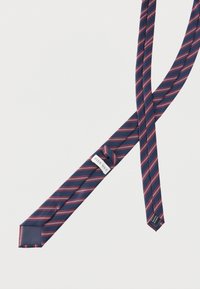 Tumesinine lips diagonaalsete punaste ja valgete triipudega, voltitud, nähtava Pier One kaubamärgiga sildi peal valgel taustal.