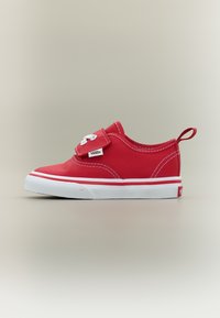 Baskets bébé Vans rouges avec semelle en caoutchouc blanche, bride à velcro, coutures blanches et languette de tirage au talon sur un fond neutre.