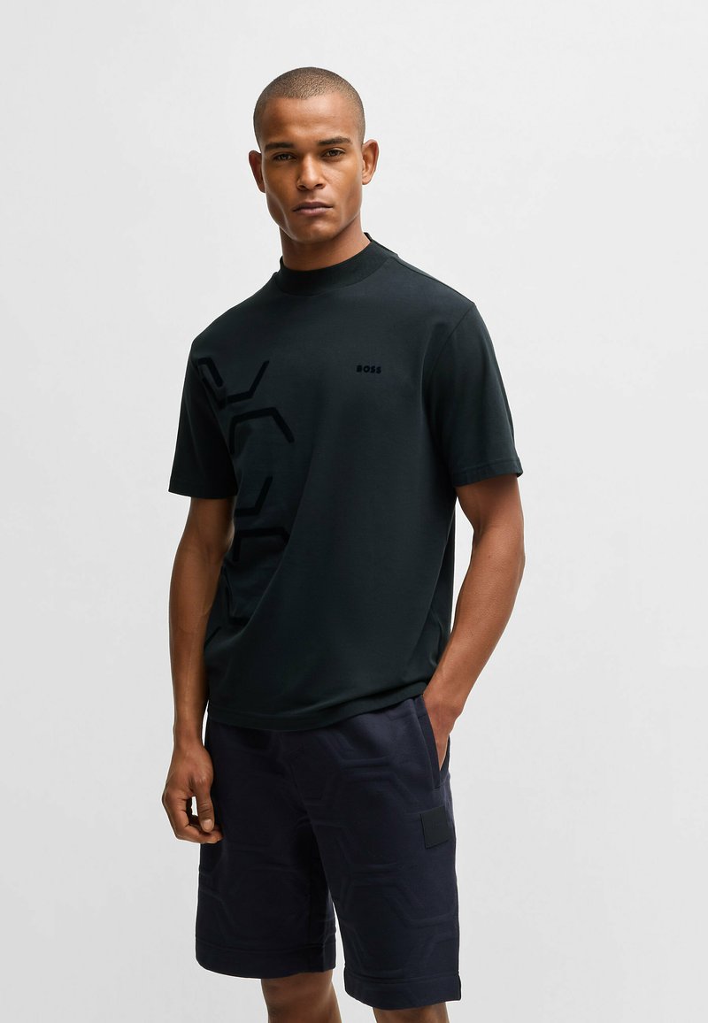 T-shirt noir à manches courtes avec un design en relief discret, associé à un short bleu marine à motifs avec poches latérales et une pièce.