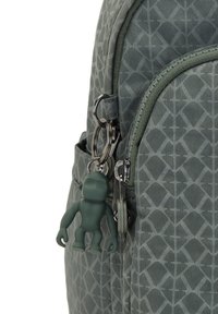 Mochila verde con estampado, superficie texturizada, cremalleras plateadas y un llavero de personaje de dibujos animados verde como adorno.