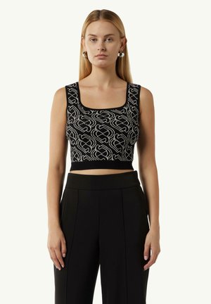 Schwarzes Cropped-Top mit quadratischem Ausschnitt, das ein weißes, ineinander verwobenes Muster aufweist. Glatte Textur. Kombiniert mit hochgeschnittenen schwarzen Hosen.