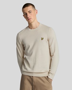 Pulover beige deschis cu gât rotund, mâneci lungi, mansete și tiv cu dantelă, având un mic logo cu o pasăre galbenă pe piept.