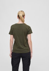 Olivenfarget t-skjorte med korte ermer og rund hals, laget av myk stoff, sett fra bak, sammen med svarte cargo-bukser.