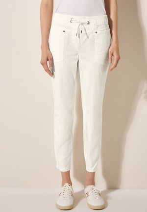 Lightweight, white cargo pants with an elastic waistband, drawstring, two front pockets, and cuffed ankles, paired with white sneakers.