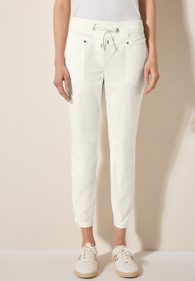 Lichte, witte cargobroek met een elastische tailleband, koord, twee voorzakken en opgerolde enkels, gecombineerd met witte sneakers.