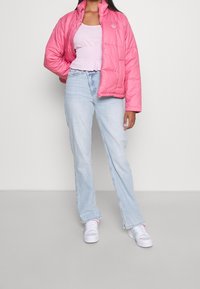 Rosa puffjacka med en glänsande yta, elastisk nederkant och broderad logotyp. Kombinerad med ljusblå högmidjade jeans och vita sneakers.