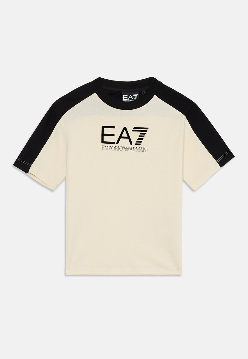 Tej anyagú, krémszínű póló fekete raglán ujjal, melyen az "EA7 Emporio Armani" logó fekete és ezüst hímzéssel látható. Szokásos környakú fazon.