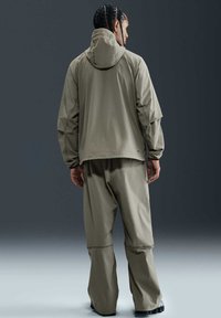 Lätt, andningsbar jacka i olivgrön med huva, kombinerad med matchande löst sittande byxor. Har en sportig design och elastiska ärmslut.