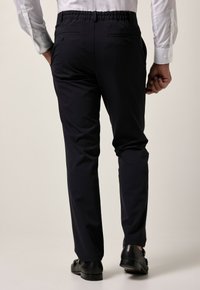 Donkerblauwe broek met een elastische tailleband, twee achterzakken, rechte pijpen en een gladde stoftextuur. Gemaakt met zwarte schoenen.