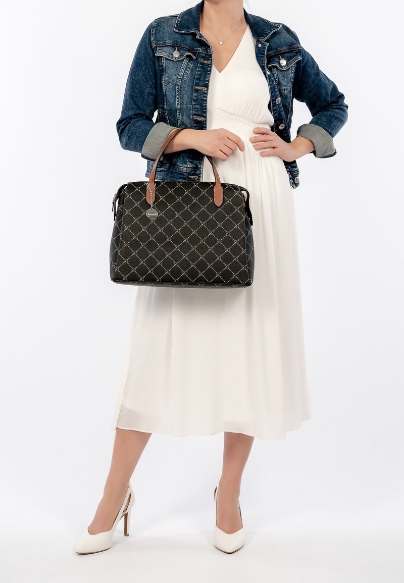 Black handbag with a quilted pattern, brown leather handles, silver hardware, and a logo charm. Worn with a denim jacket and white dress.