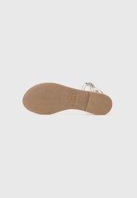 Beige rubberen zool van een sandaal met textuurhobbels, voorzien van een zilveren strap en een decoratieve kettingdetail op de bovenkant.