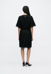 Czarna sukienka o miękkiej fakturze, z krótkimi rękawami, dopasowaną talią i długością do kolan, zestawiona z czarnymi szpilkami.