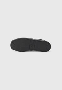 Black rubber shoe sole with textured grip pattern and raised logo. Features pointed heel and rounded toe for stability and support.