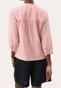 Blusa de lino a rayas rojas y blancas con mangas tres cuartos, con la parte trasera fruncida y puños abotonados, combinada con pantalones cortos negros.