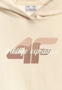 Sweat à capuche beige avec logo "4F" et texte "Wildlife expedition", taille 140, l'étiquette indique conçu en Europe, fabriqué au Bangladesh.
