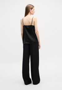 Svart sateng-camisole med tynne stropper, løs passform og en glatt tekstur. Kombinert med høyhårede svarte vide bukser.
