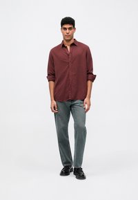 Tumši sarkans krekls ar uzrollētām piedurknēm, savienots ar gaiši pelēkiem džinsiem un melnām kurpēm. Gluda auduma ar brīvu piegriezumu.