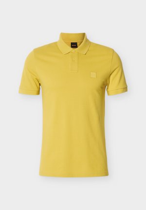 Rumena bombažna polo majica s klasičnim ovratnikom, kratkimi rokavi in tonirano logotipno našivko na prsih. Gladek tekstura, enobarvna.