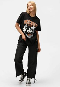 Camiseta negra de algodón con un gran gráfico de Mickey Mouse; combinada con pantalones cargo negros y zapatillas negras con acentos blancos.