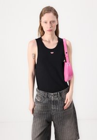 Svart ermeløs tanktop med liten rød logo, kombinert med grå stripete vide shorts og en skinnende rosa håndveske.