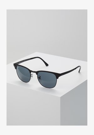 Mustat aurinkolasit tummanharmailla linsseillä. Varustettu ohuella metallikehyksellä ja huomaamattomalla brändäyksellä sivussa, klassinen muoto ja malli.