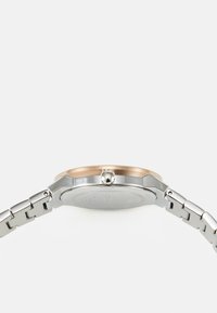 Silberne und roségolden Uhr mit runder Gehäuseform, achteckiger Form, Metallarmband und einem Kronen-Detail an der Seite. Flacher, glatter Rücken.