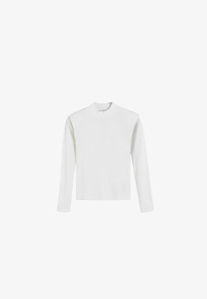 Weißes Langarmoberteil mit hohem Kragen, gerippter Textur und geradem Schnitt, minimalistisch gestaltet und ohne sichtbare Hardware.