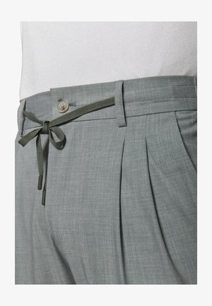 Jasnoszare spodnie z plisami, zapinane na guziki, z szlufkami na pasek i materiałowym wiązanym sznurkiem w talii, noszone z białą koszulą.