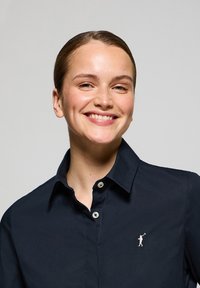 Camisa de botones azul marino con cuello, que presenta un pequeño logotipo de golfista bordado en el lado izquierdo del pecho. Tela suave y diseño de corte clásico.