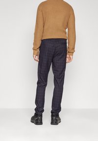 Brun stickad tröja och marinblå rutiga byxor med blå linjer. Byxorna har smal passform och är kombinerade med svarta sneakers.