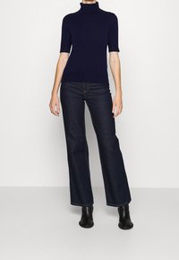 Námorně modrý svetřík s krátkým rukávem a rolákem, doplněný tmavě modrými širokými džíny, akcentovaný jemným švem a černými kotníkovými botami.