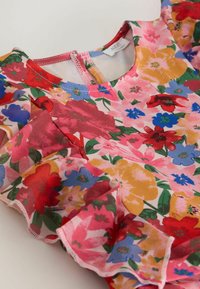 Virágos ruha rózsaszín alapon; piros, sárga és kék virágok díszítik. Rövid fodros ujjú, hátul cipzárral záródik. Puha anyagból készült.