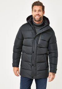 Schwarze Puffjacke. Mit einem Reißverschluss und Knopfverschluss, einer Kapuze und gerippten Bündchen. Das Material ist glatt mit einer plüschigen, gesteppten Textur.
