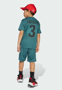 Completo sportivo Adidas turchese con design a ragnatela nera e numero 3 sul retro, abbinato a un cappellino rosso e scarpe nere e rosse.