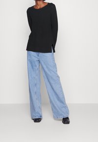 Maglia nera a maniche lunghe con scollatura rotonda e spacchi laterali, abbinata a jeans a gamba larga blu chiaro e scarpe nere con tacco a blocco.